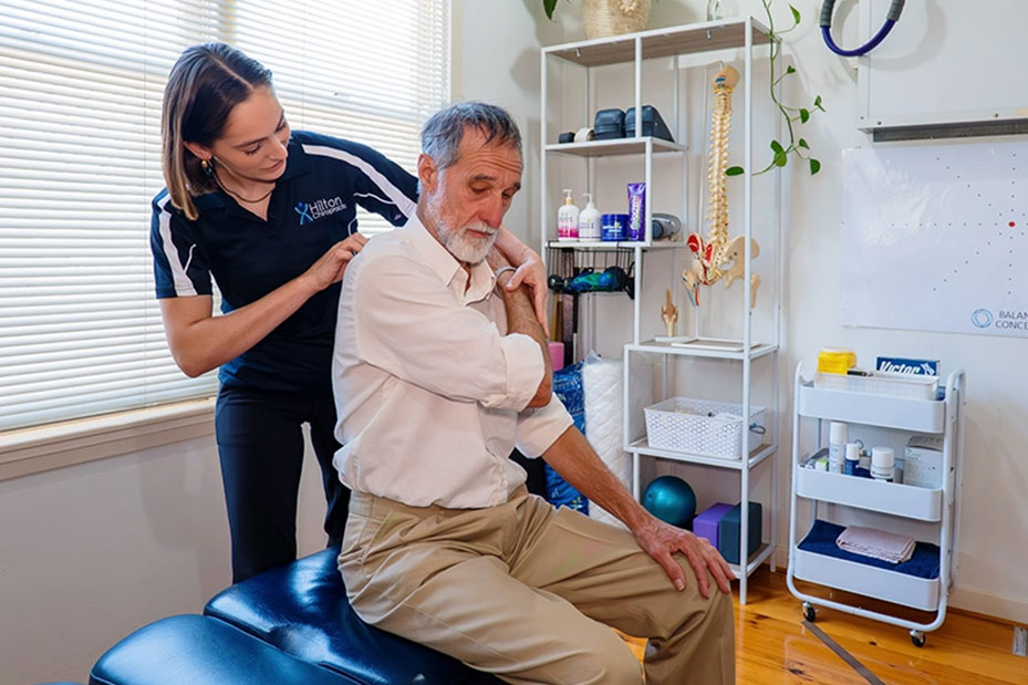 A man receives a shoulder examination from a physical therapist in a clinical setting
